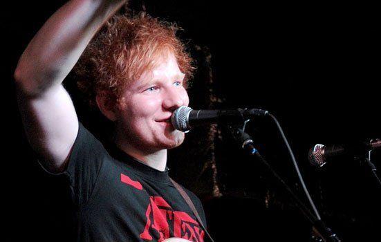 Ed Sheeran sorride sul palco davanti al microfono