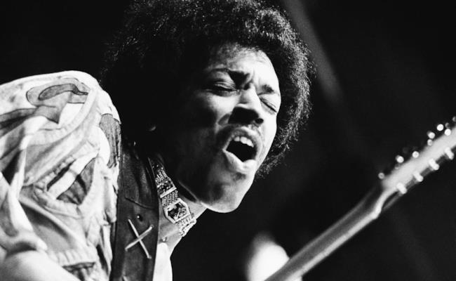 Immagine in bainco e nero di Jimi Hendrix con la chitarra in mano ad un concerto negli anni '60 