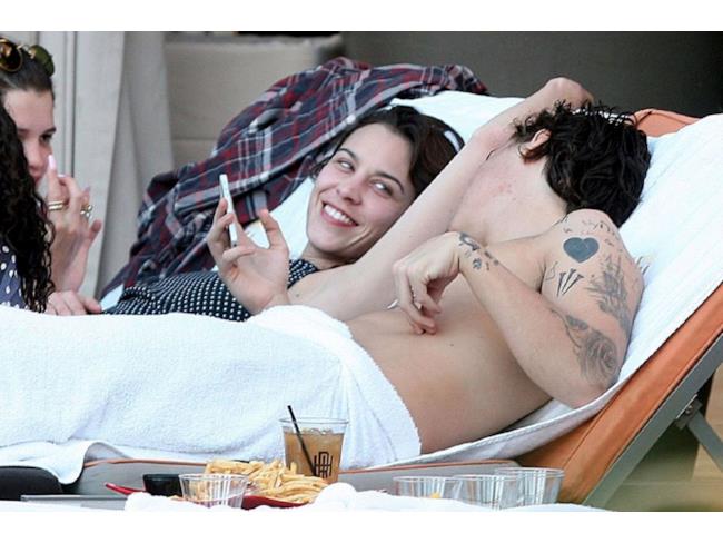 Harry Styles controlla il cellulare mentre si rilassa su di una sdraio.