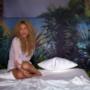 La riccia Shakira canta da un letto circondato da palme e disegni di paesaggi tropicali