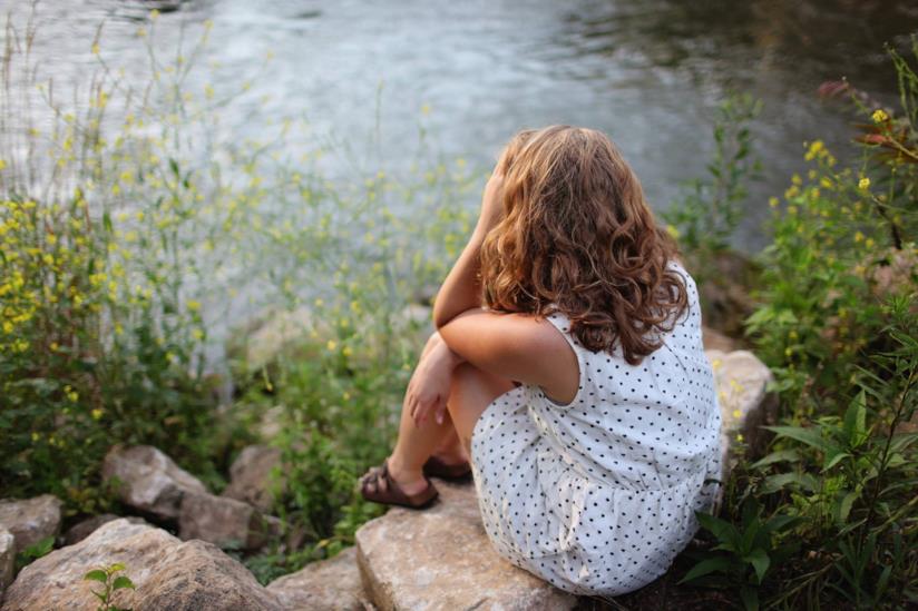 Frasi sulla vita dura Ragazza seduta sul bordo di un lago con le mani sul volto