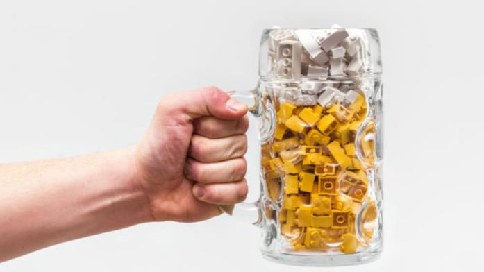 Primo piano di una mano che impugna un boccale di birra contenente mattoncini LEGO