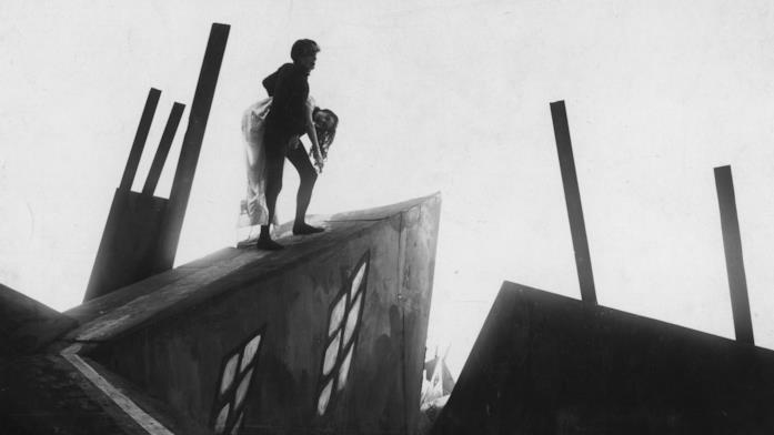 Una scena da Il gabinetto del Dottor Caligari Un uomo tiene tra le braccia una donna incosciente in una scenografia spigolosa e surreale