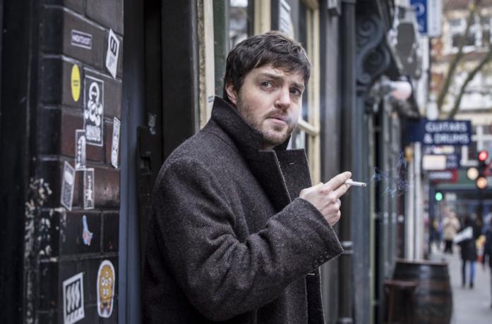 Tom Burke fuma in una scena della serie TV Strike