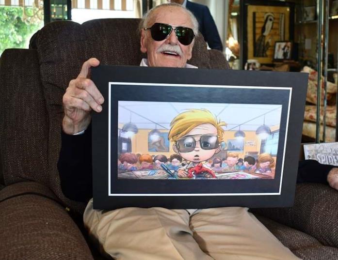 Un primo piano di Stan Lee con in mano un'illustrazione che lo raffigura bambino