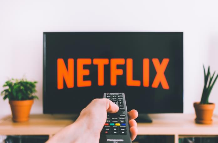 Il logo di Netflix in un televisore e un utente con un telecomando
