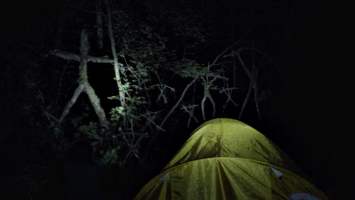 The Blair Witch Project, di Daniel Myrick ed Eduardo Sánchez (1999) Una scena notturna di finto found footage con una persona di spalle di fronte ad un'inquietante scultura rudimentale di rametti