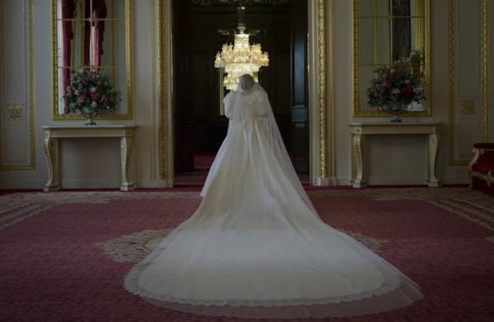 Emma Corrin è Lady Diana Spencer, nella quarta stagione di The Crown Lady Diana Spencer, con un abito bianco, cammina all'interno della lussuosa residenza