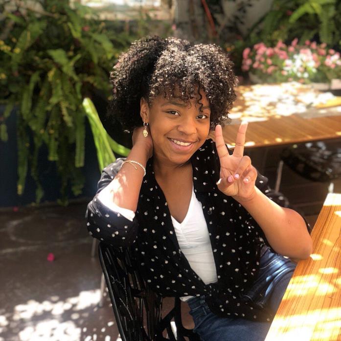 Priah Ferguson, oggi 13enne Priah Ferguson seduta a un tavolo sotto il sole, che fa il gesto della vittoria