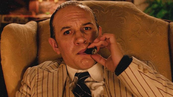 Tom Hardy nei panni di Al Capone Capone fuma un sigaro seduto sulla propria poltrona