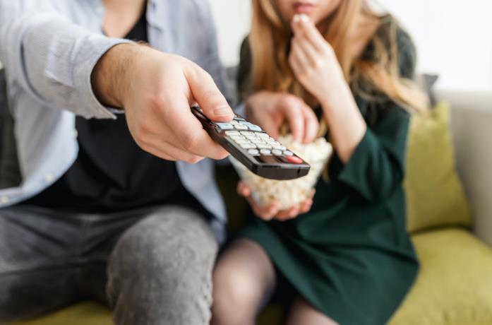 Un ragazzo usa il telecomando, mentre la ragazza mangia popcorn