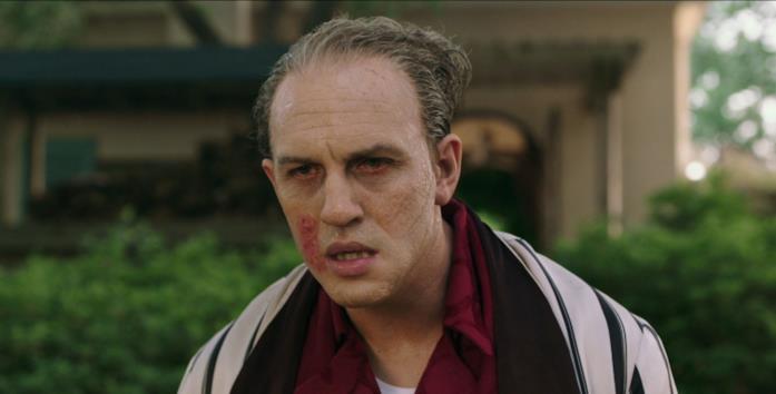 Tom Hardy in Capone Capone, col viso distrutto dalla neurosifilide, passeggia in vestaglia nel proprio giardino