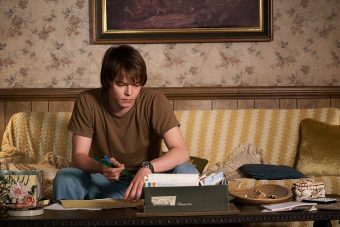 Charlie Heaton in Stranger Things 1 Charlie Heaton nei panni di Jonahtan Byers, seduto sul divano con una penna in mano