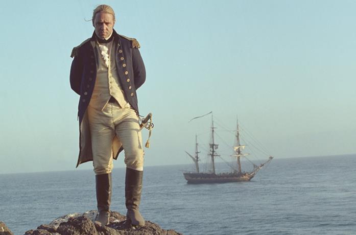 Il protagonista del film su uno scoglio, con la sua nave in lontananza
