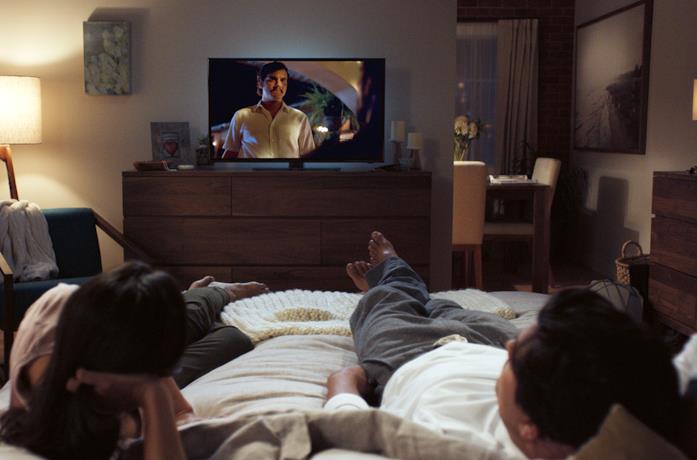 Una coppia sdraiata sul letto guarda la TV
