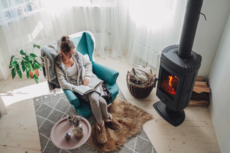 Donna legge in poltrona vicino a una stufa a legna accesa