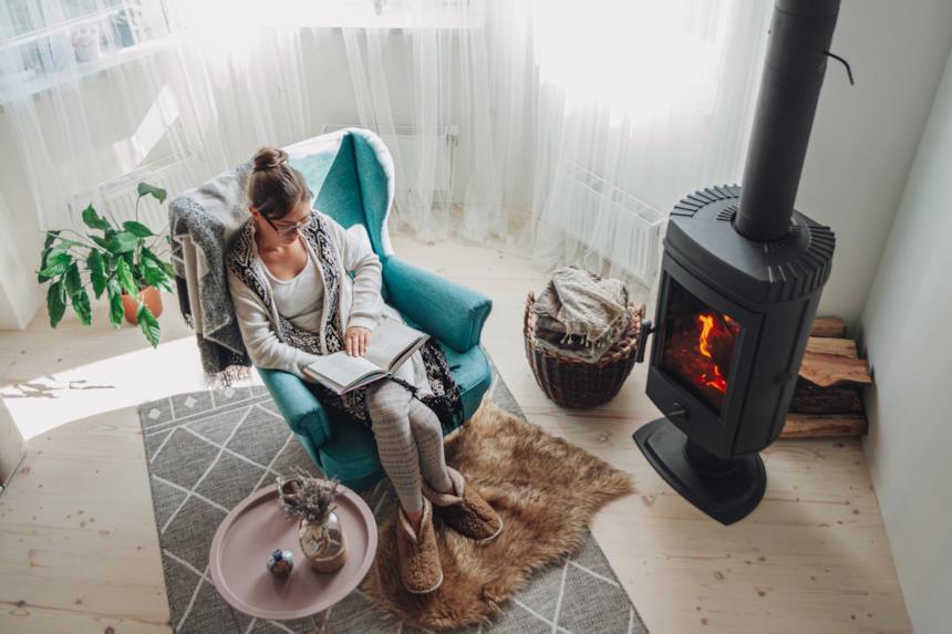 Donna legge in poltrona vicino a una stufa a legna accesa 
