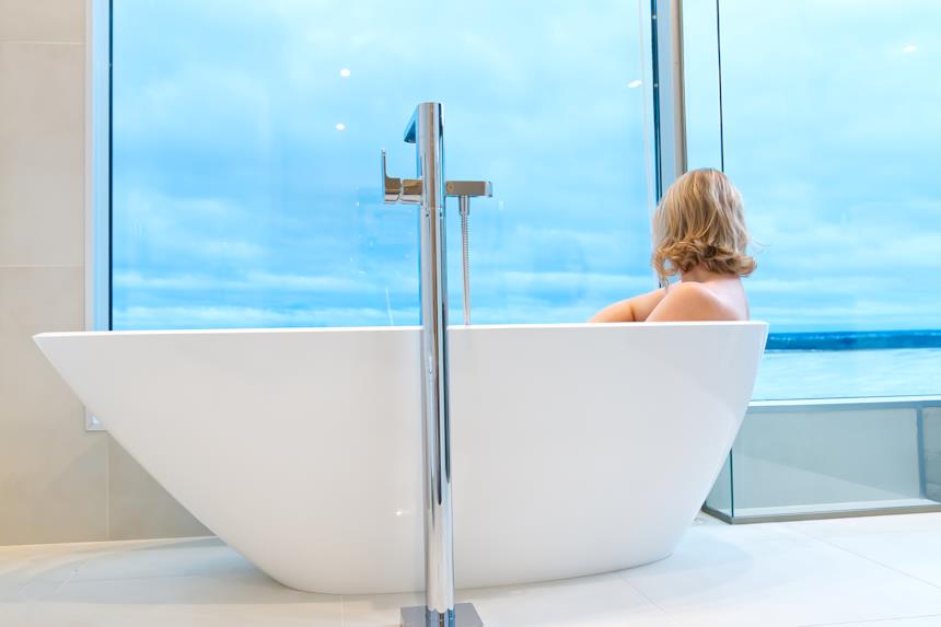 Donna si rilassa nella vasca da bagno guardando il mare da una vetrata 