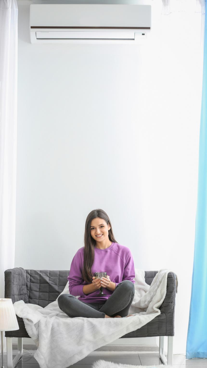 Ragazza sul divano con un climatizzatore a parete sopra di lei