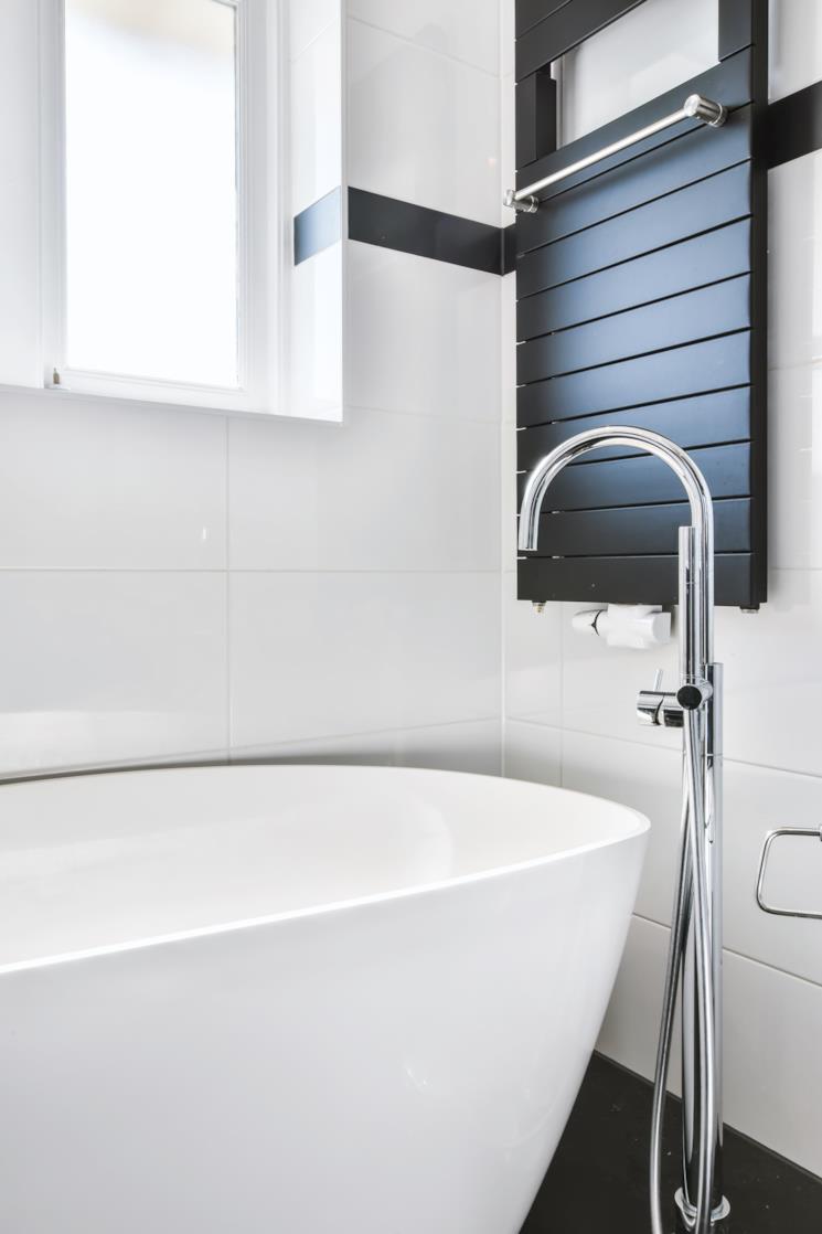 Termoarredo nero collocato dietro una vasca freestanding