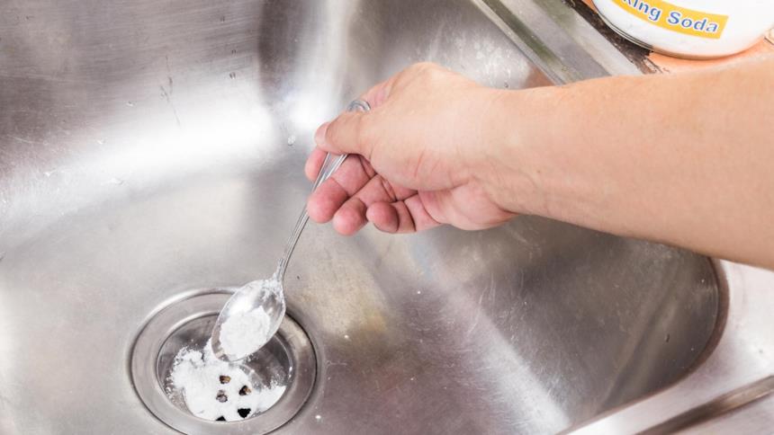 Dettaglio della mano di un uomo che versa la soda caustica nello scarico del lavandino