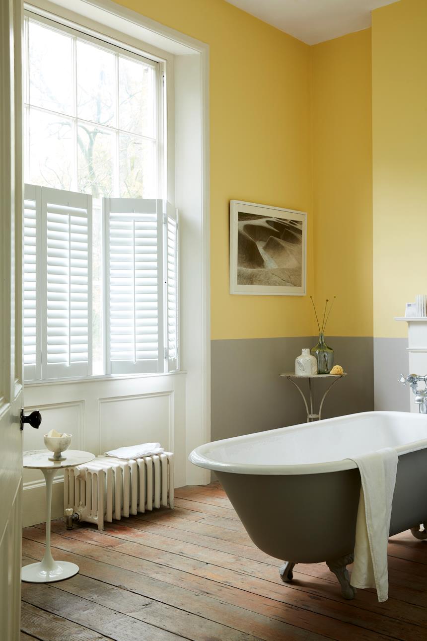 Bagno con parete metà gialla e metà grigia e pavimento in parquet