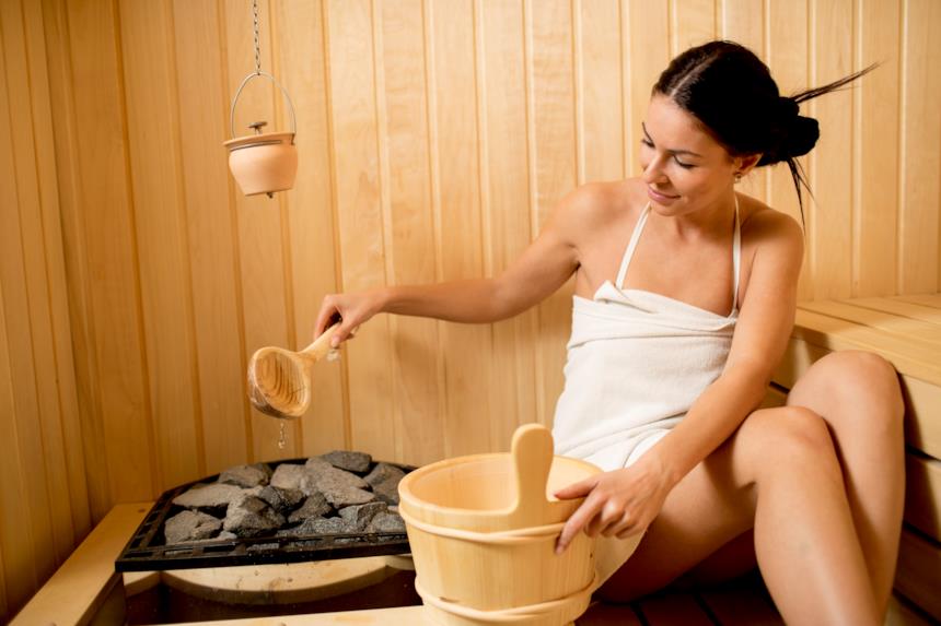 Ragazza versa l'acqua sul braciere in sauna 