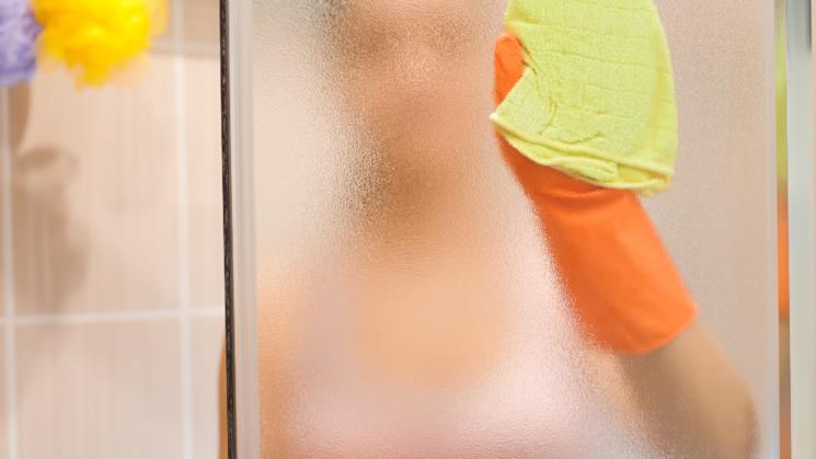 Donna pulisce le pareti del box doccia