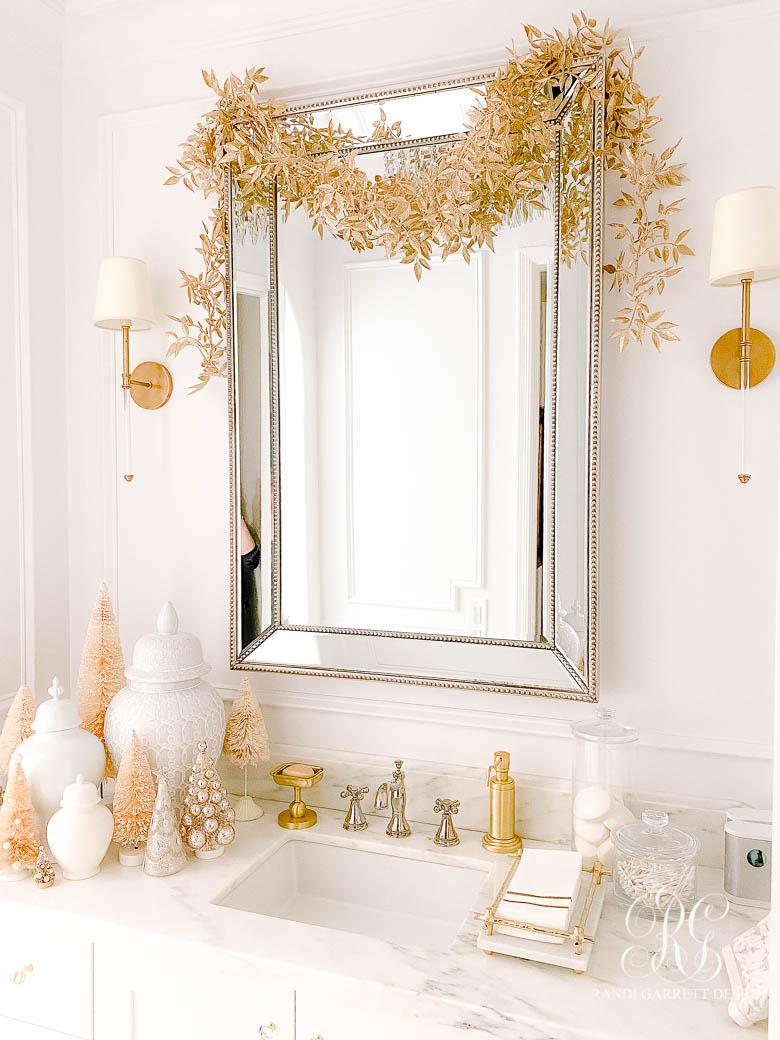 Foto di uno specchio decorato con un nastro oro e di un lavello con addobbi natalizi oro