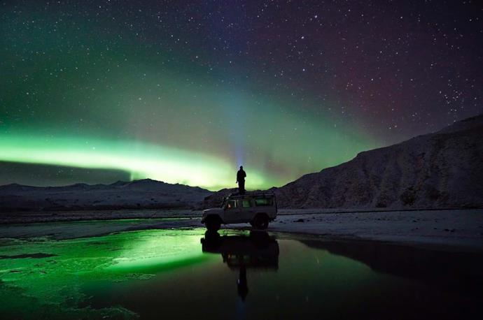 Man standing on a car while admiring the nothern lights