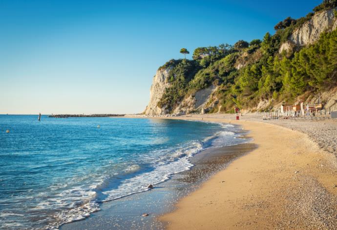 Spiaggia lungo la Riviera del Conero delimitata da rocce punteggiate di macchia mediterranea