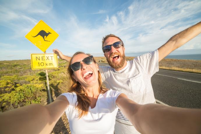 Primo piano selfie di una coppia di ragazzi con alle spalle un cartello che segnala la presenza di canguri