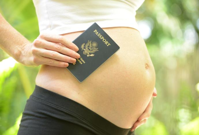 Un passaporto sul pancione di una donna incinta
