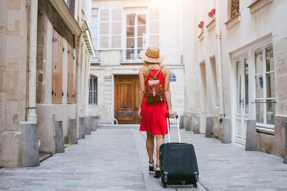 Ragazza di spalle in abito rosso con valigia